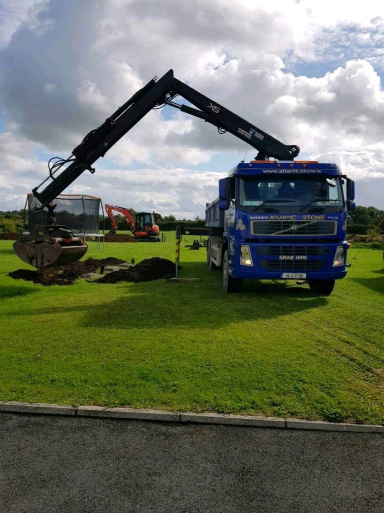 Grab lorry delivering topsoil to low spots in a domestic garden lawn in Mayo. Levelling topsoil with a mini digger in the background.